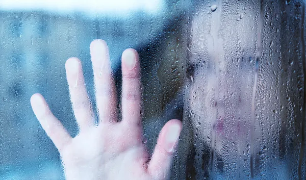 Меланхолия и грустная молодая женщина в окне в дожде Стоковое Изображение