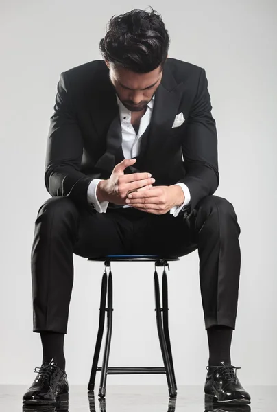 Man in tuxedo looking down while sitting on a stool, — стоковое фото