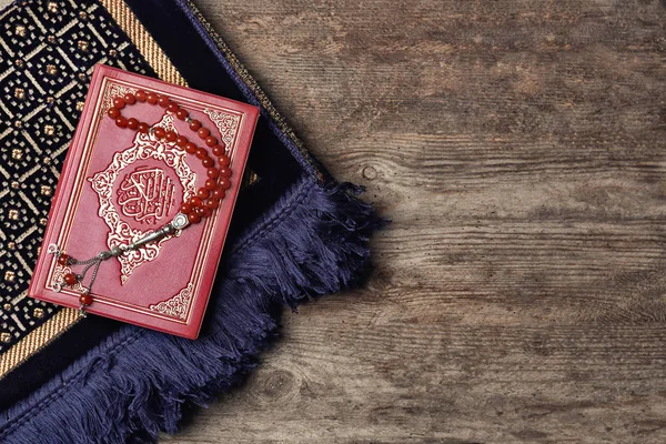 Священная книга мусульман, четки и ковер на деревянных фоне — стоковое фото