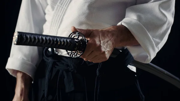 Мастер айкидо, традиционные Самурай Хакама одежде держит его японский меч в ножны. Он находится в Spotlight тьма окружает его. Выстрел, изолированные на черном фоне Лицензионные Стоковые Фото
