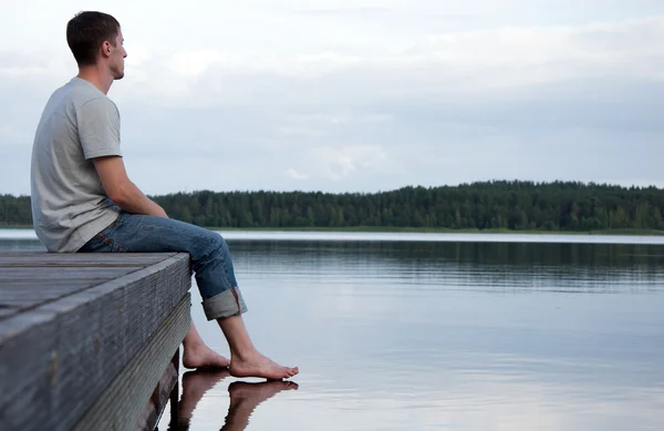 Молодой человек, сидя в одиночестве на воде Лицензионные Стоковые Фото