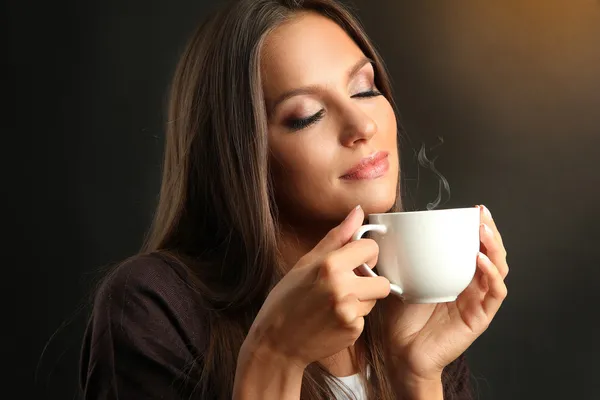 Красивая молодая женщина с чашки кофе на коричневый фон — стоковое фото