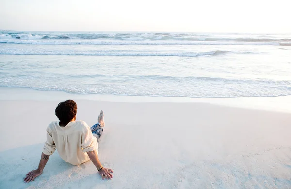 Молодой человек, сидя на пляже — стоковое фото