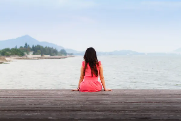Грустно женщина сидит в одиночестве на пристани — стоковое фото