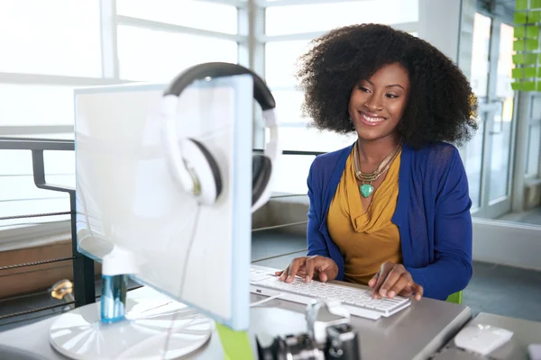 Портрет улыбается женщина с афро на компьютере в офисе ярким стекла — стоковое фото