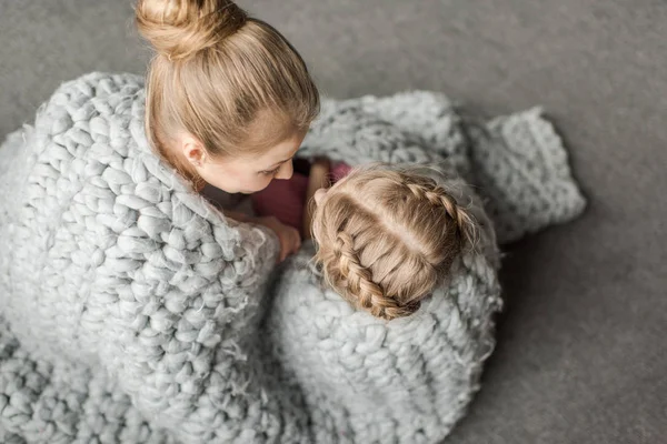 Вид сверху матери и дочери обнимает и сидит на полу с шерстяным трикотажным одеялом Стоковое Фото