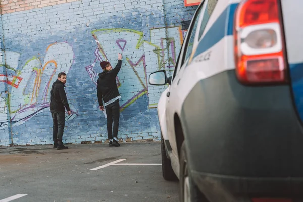 Вернуться Мнение Вандалов Живопись Граффити Стене Полицейская Машина Переднем Плане — стоковое фото